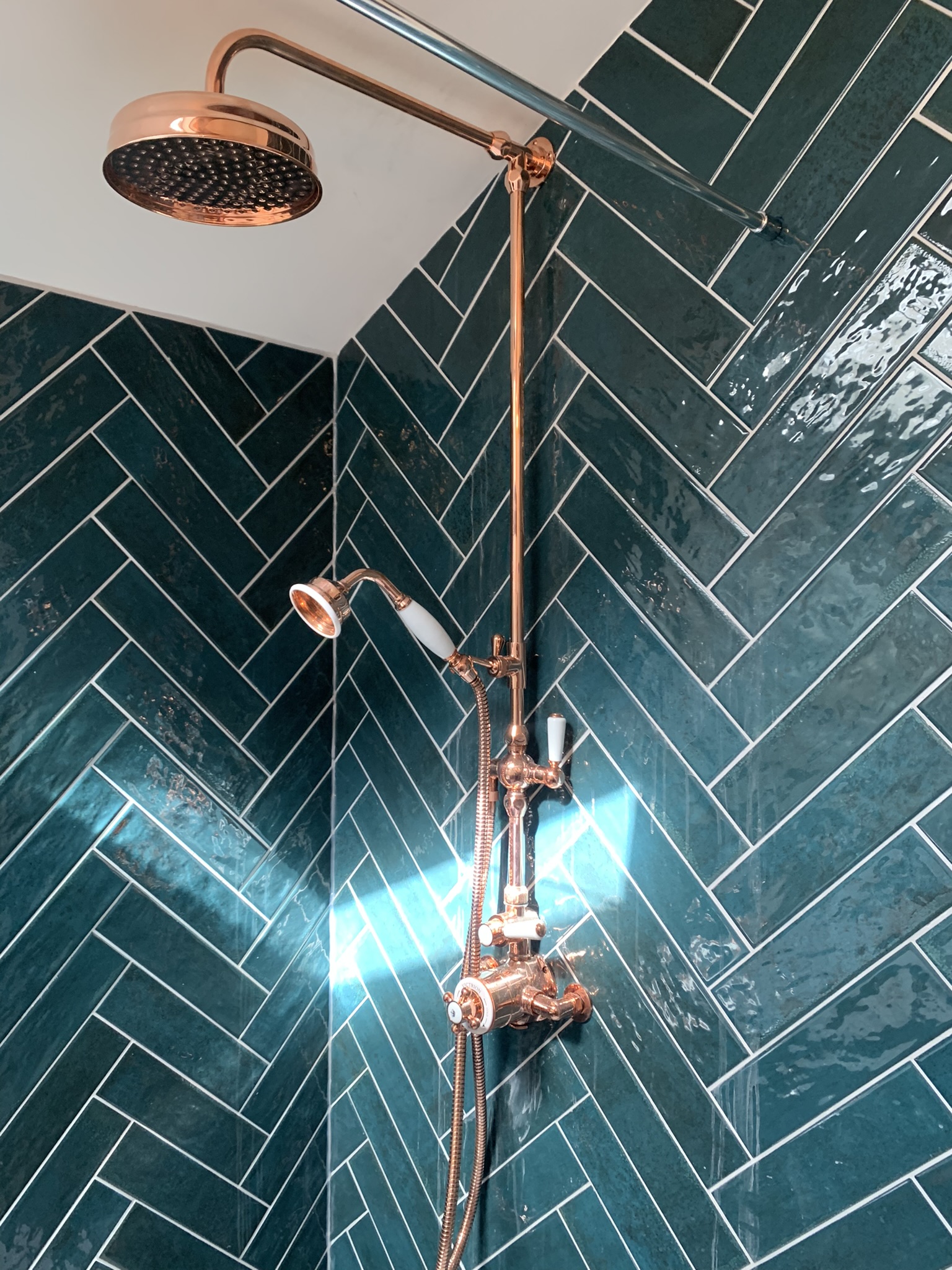 Copper rain-head shower with an exposed copper riser on dark teal herringbone tiles