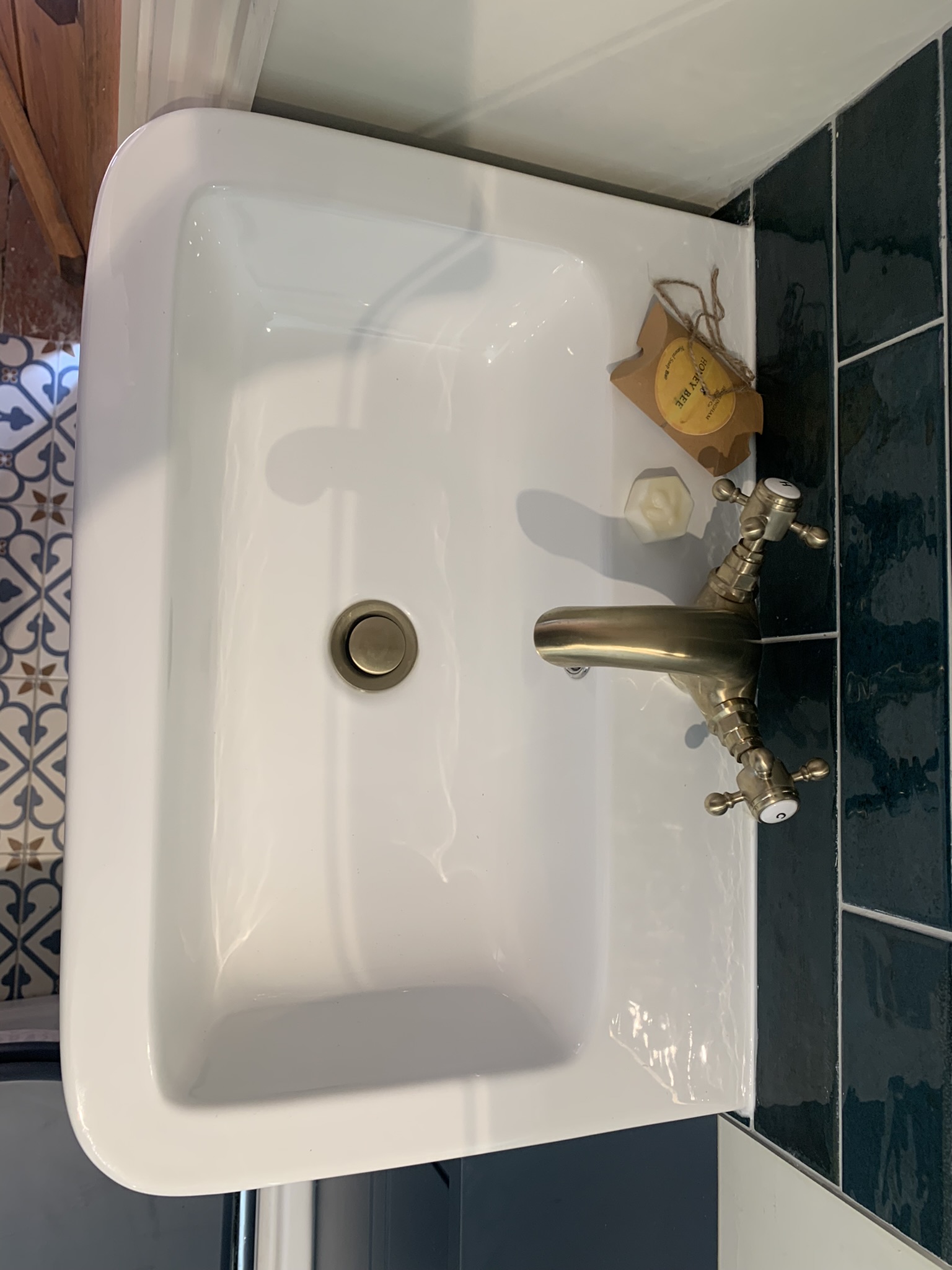 White basin with a brass mixer tap beside teal wall tiles, seen from above