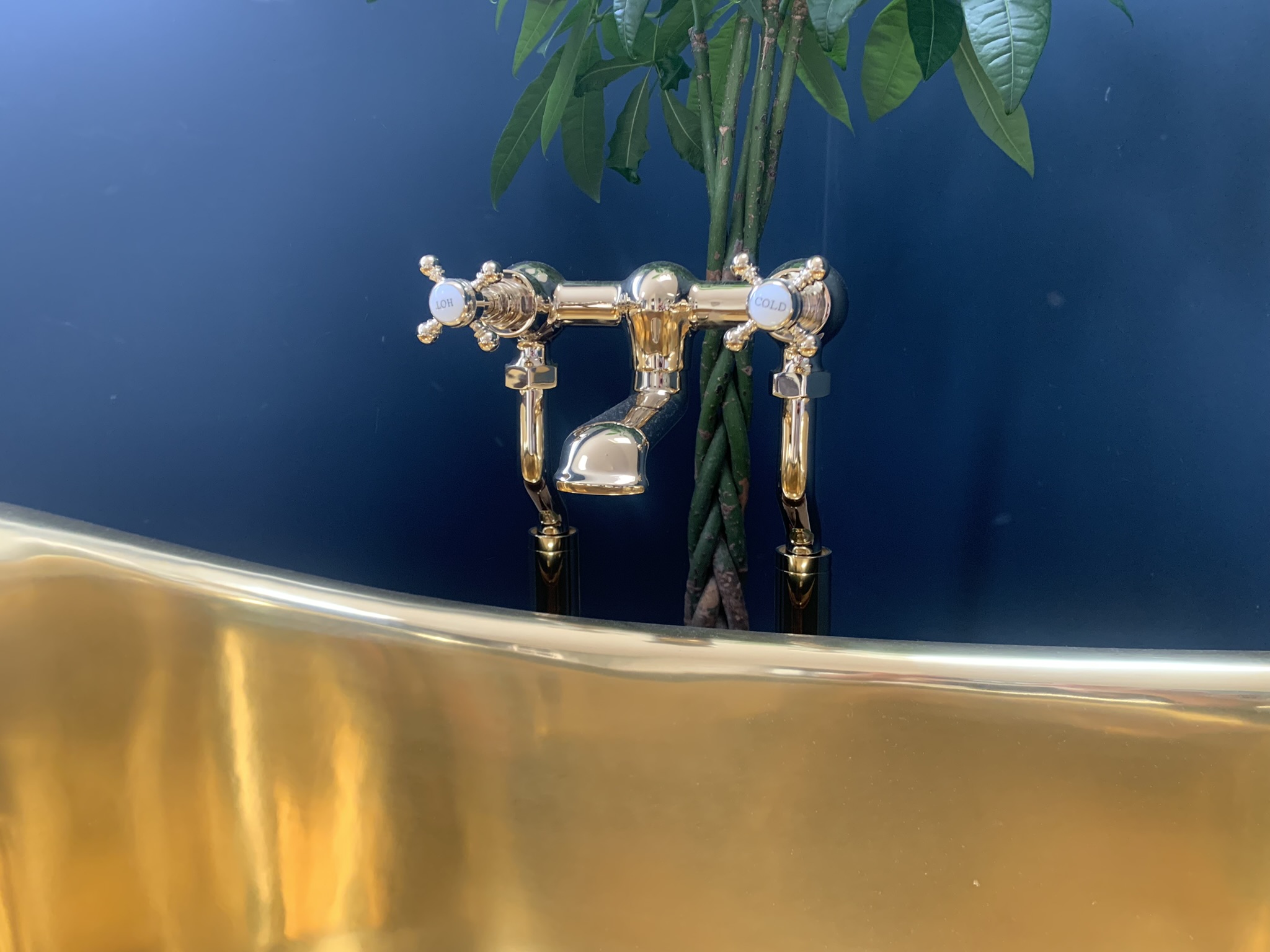 Brass bath mixer with cross-head taps over a polished brass bath against a navy wall