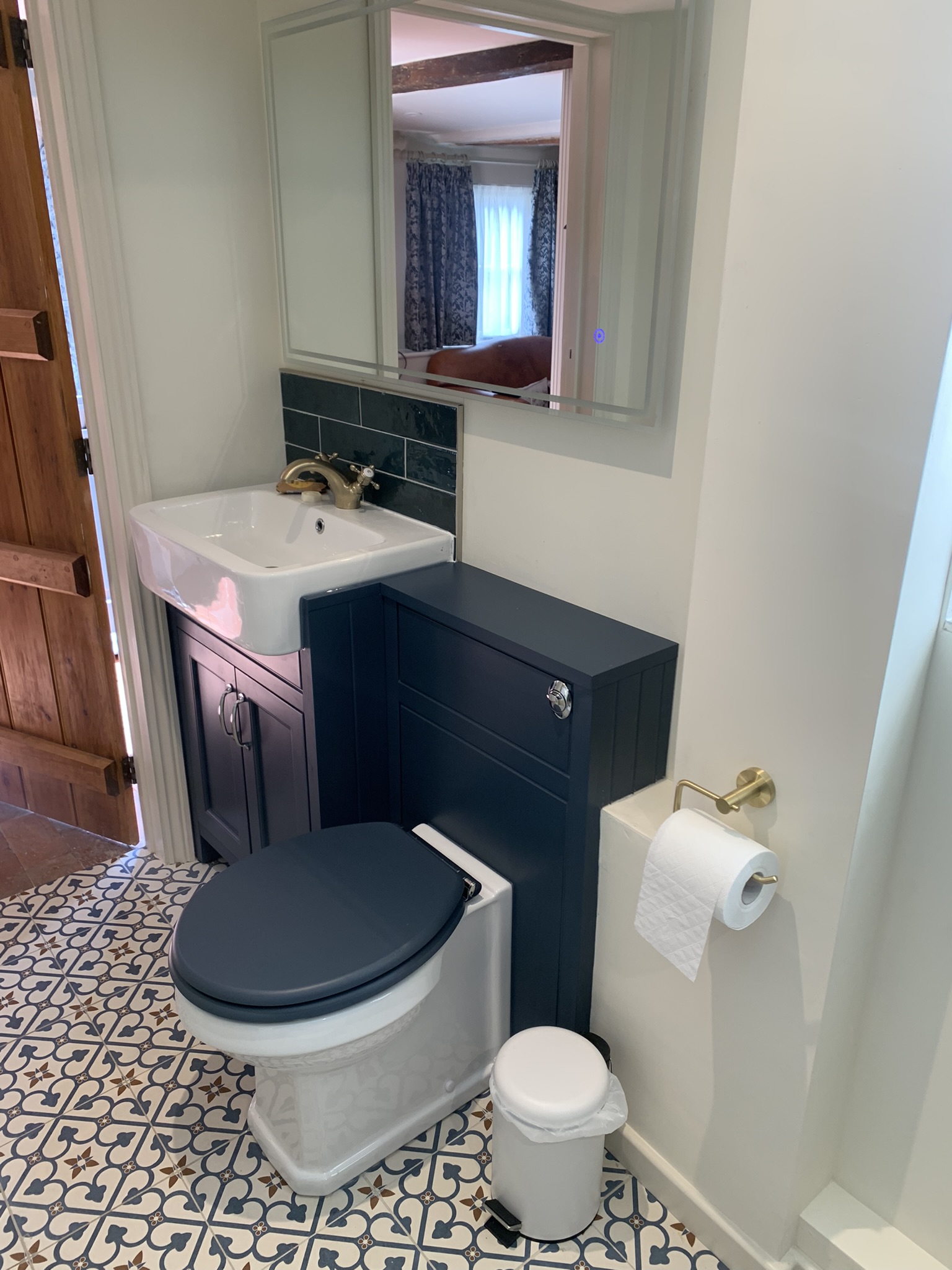Navy vanity unit and toilet with a brass basin tap on a patterned tiled floor