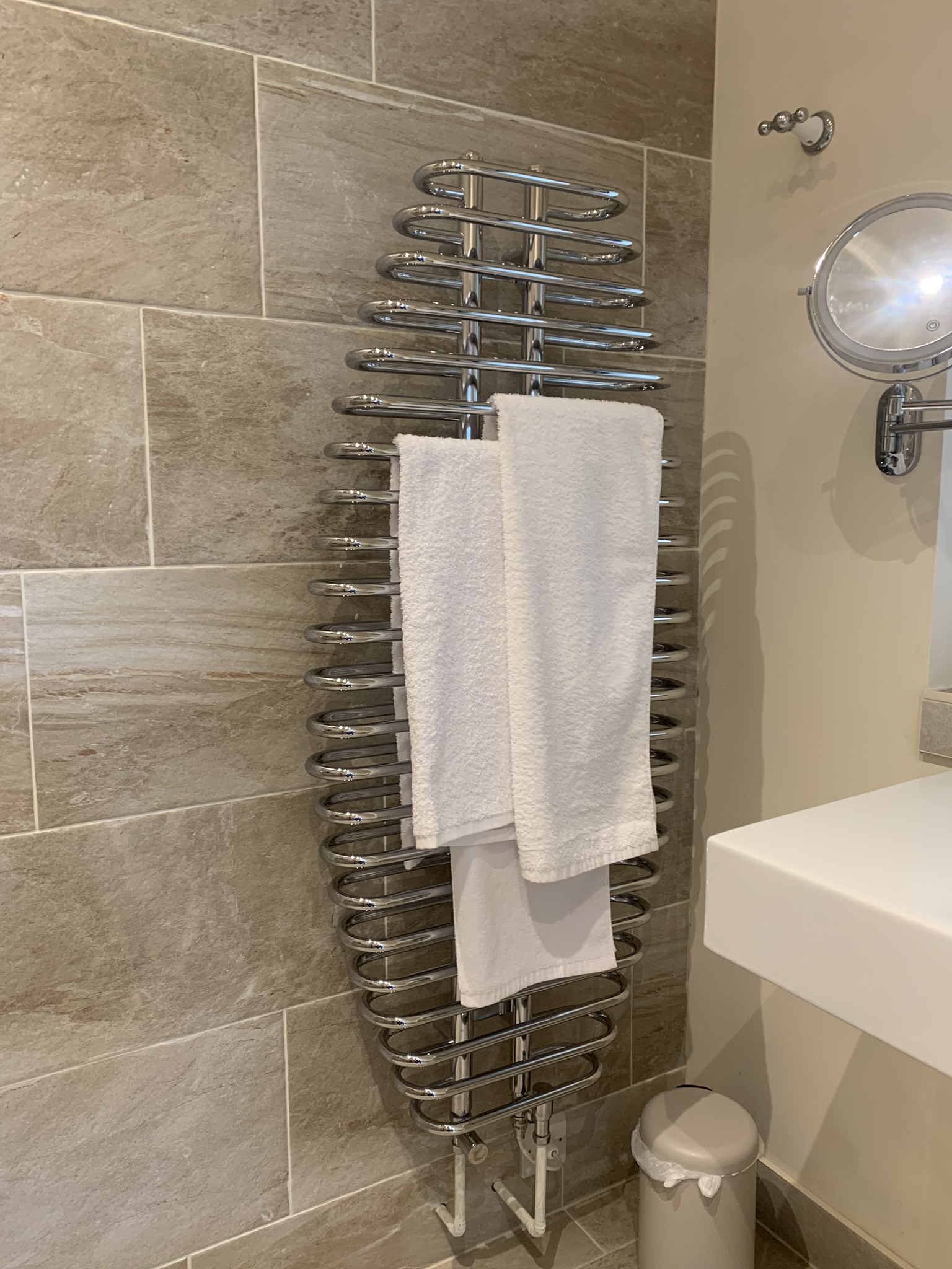 Chrome serpentine towel radiator on large stone-effect wall tiles
