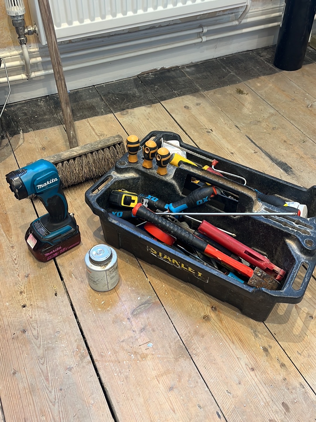 Matt's tool tray with a drill, fittings and hand tools on old floorboards by a radiator